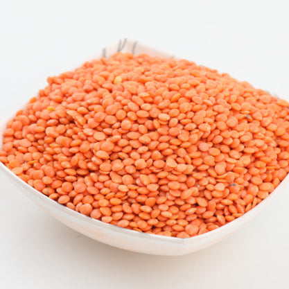 White bowl filled with red lentils on a dark surface with scattered lentils.